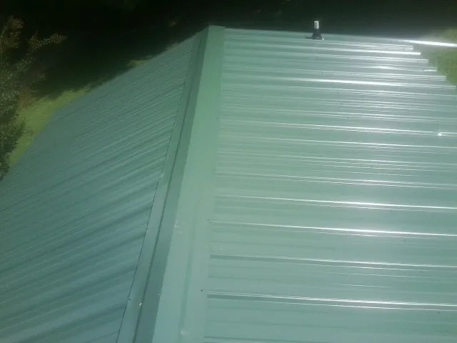 New green metal panels meeting at the ridge of a roof — Flat Roof Repair work by our crew in Manahawkin