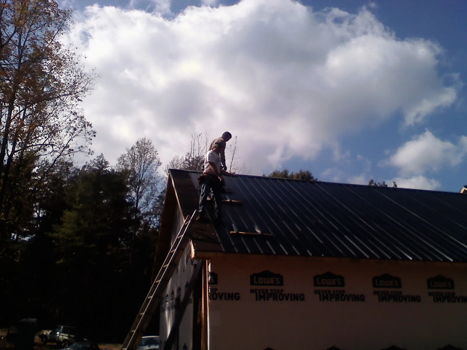 Roofer fastening dark metal panels high against a cloudy sky, from a Roof Inspection job in Manahawkin