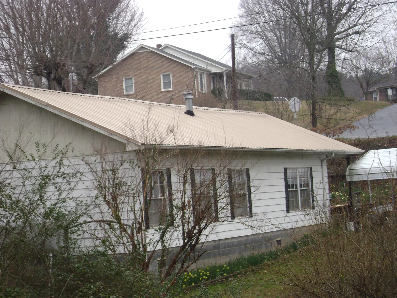 Tan metal roof on a white sided house set into a hillside — Commercial Roofing by Roofing Brothers in Manahawkin